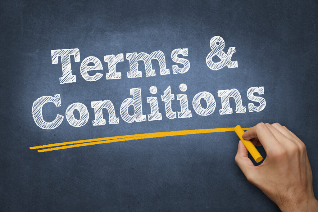 A hand holding a yellow chalk draws a line beneath the chalkboard-style text "Terms & Conditions" written in white on a dark blue background.